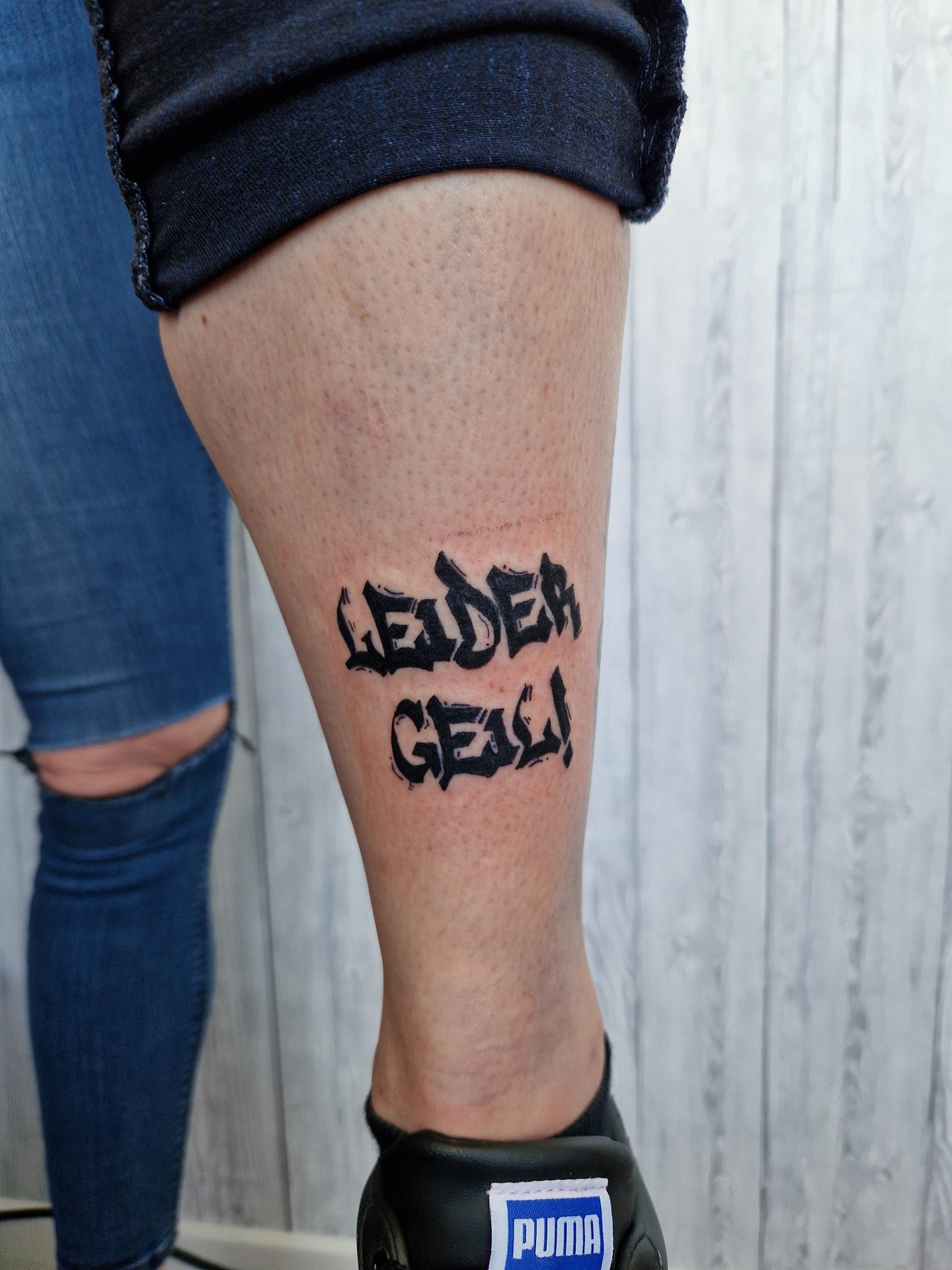 Lettering-Tattoo „Leider geil!“ am Wadenbein